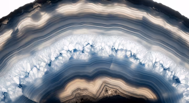 A polished slice of agate showing its intricate, concentric bands of blue, white, and grey.